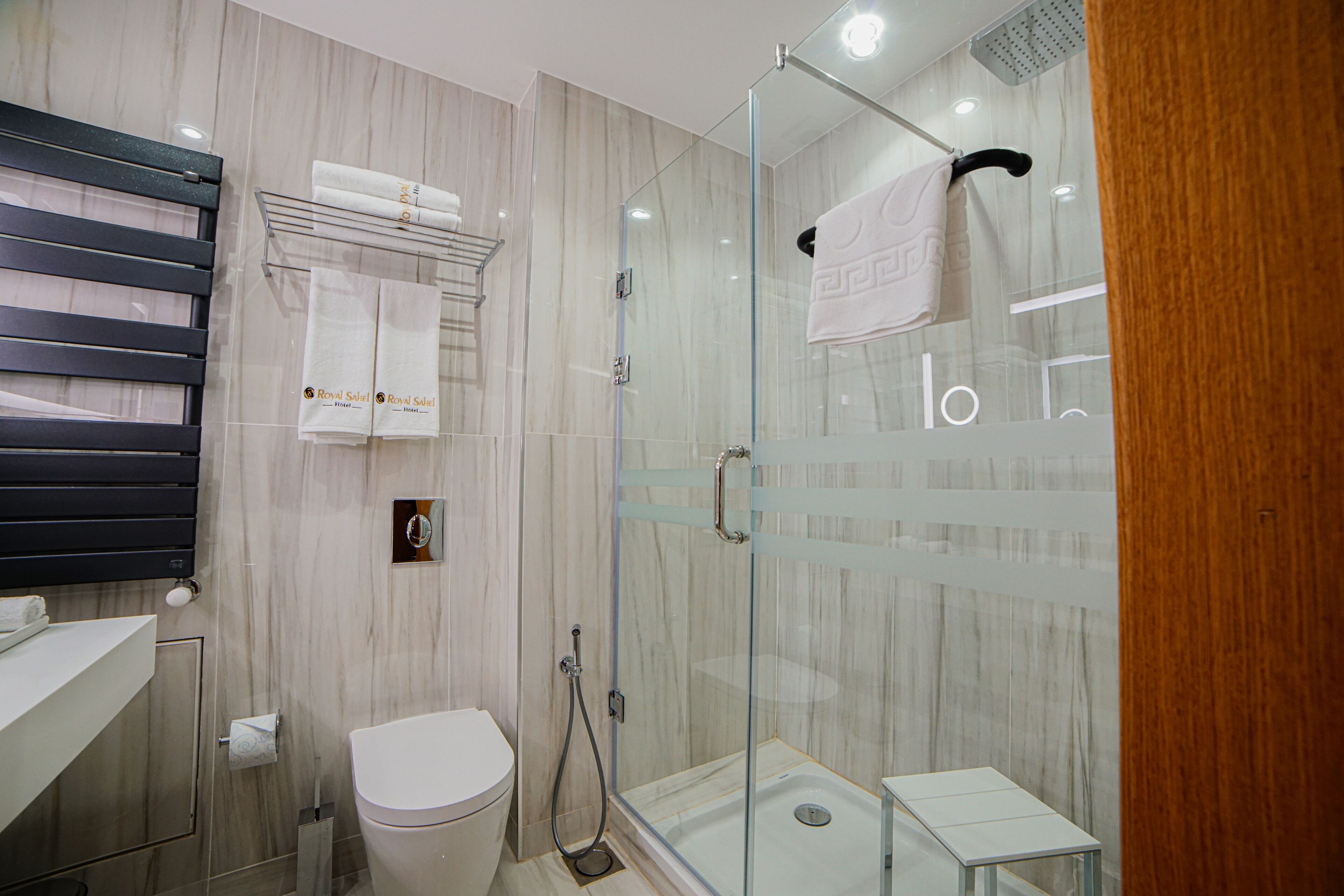 Un baño moderno con ducha de vidrio, inodoro y toallero con toallas dobladas.