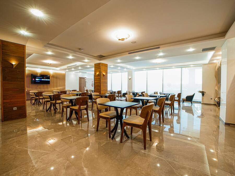 A spacious dining area with multiple tables and chairs, a flat-screen TV mounted on the wall, and large windows allowing natural light.