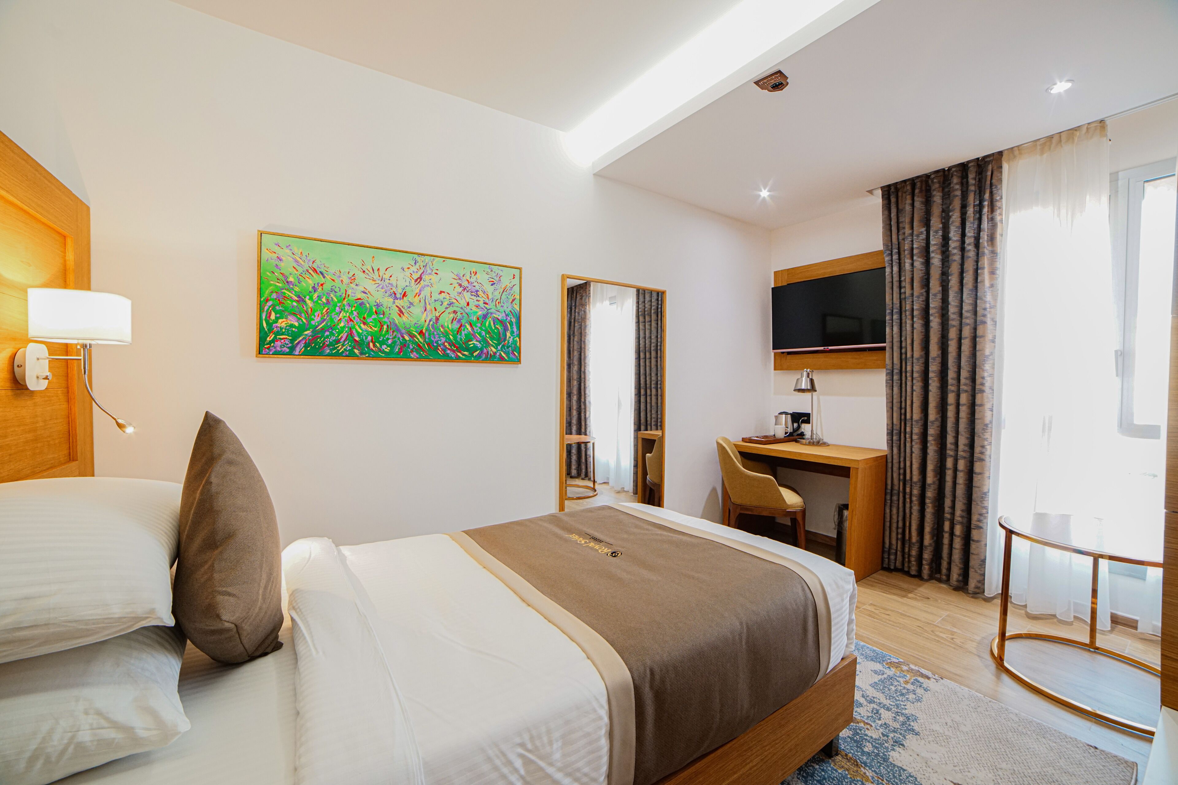 Habitación de hotel con cama, escritorio, silla, televisión y un cuadro en la pared.