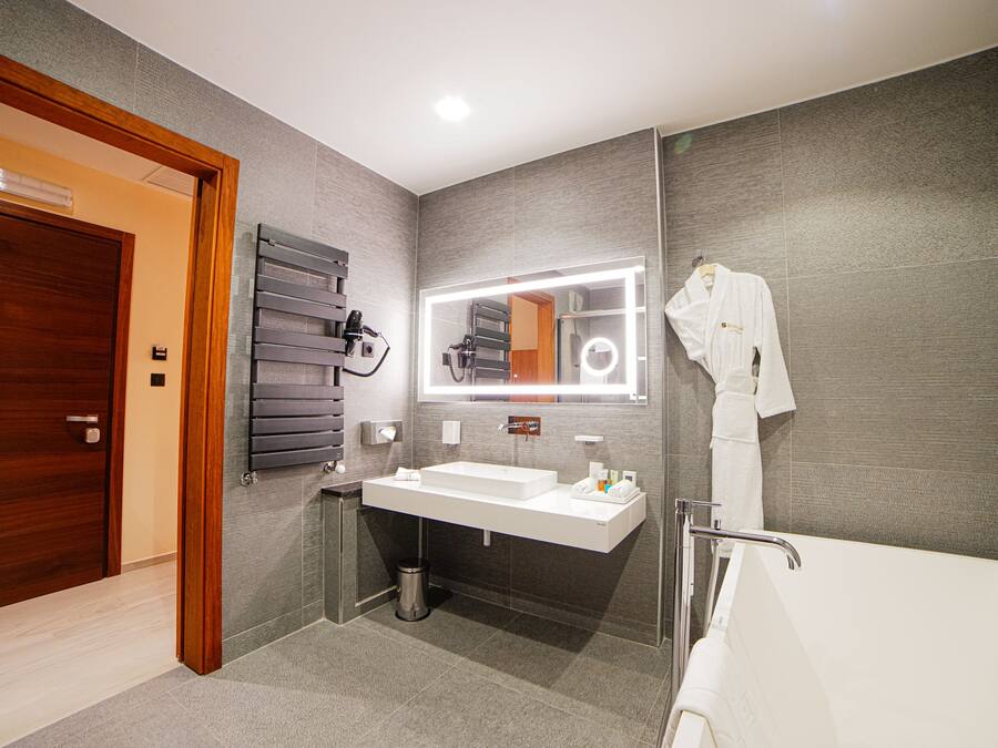 Un baño moderno con puerta de madera, un espejo grande con iluminación, un lavabo blanco y una bañera.