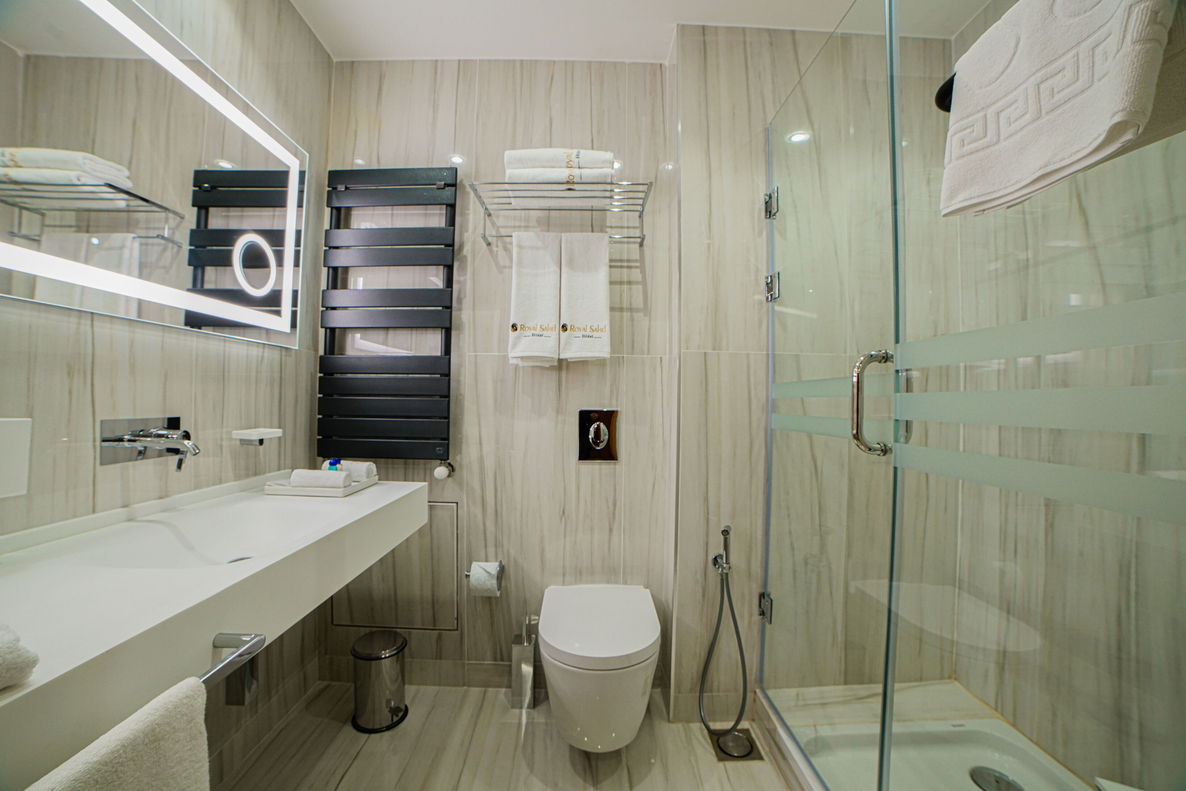 Un baño moderno con cabina de ducha de vidrio, inodoro blanco y tocador con espejo y perchero.