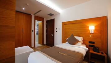 Habitación de hotel con una cama grande, armario de madera, mesita de noche con lámpara y una pequeña mesa con teléfono.