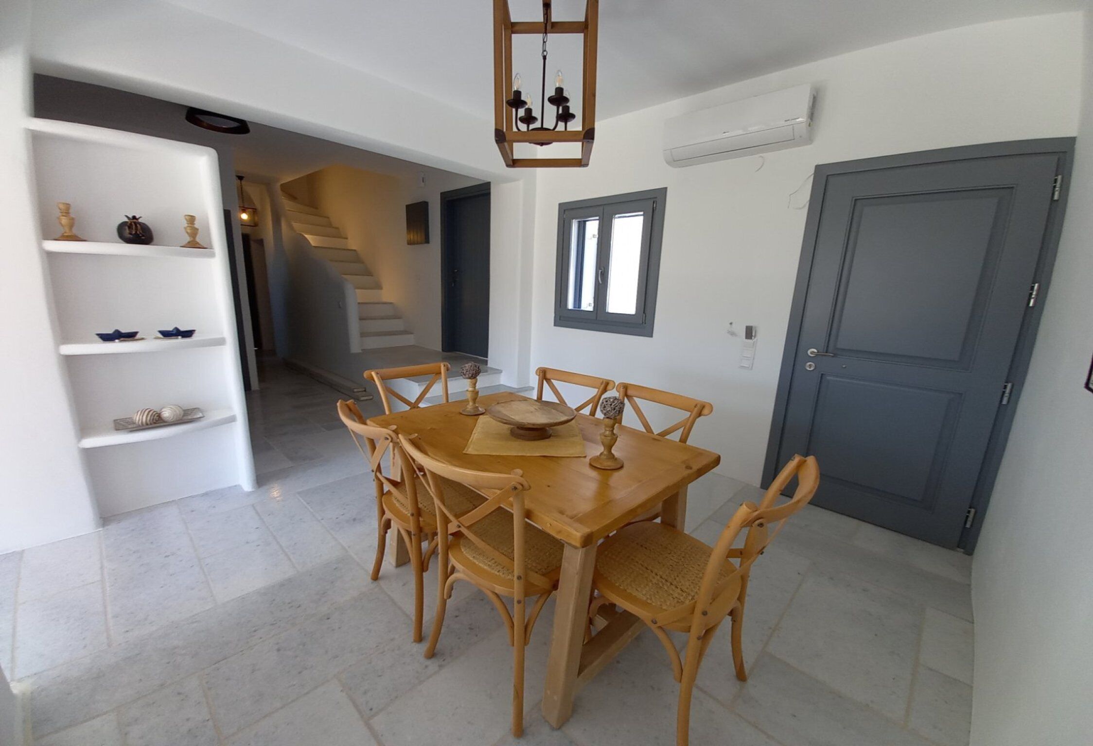 A dining area with a wooden table and chairs, a chandelier, and a staircase in the background.