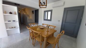 A dining area with a wooden table and chairs, a chandelier, and a staircase in the background.