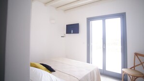 A bedroom with a bed, a chair, a TV mounted on the wall, and a sliding glass door. - Krotiri View of  Paros (Paros)