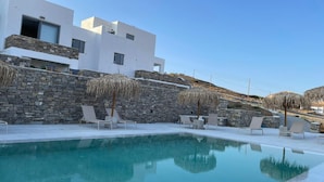 A modern building with a pool, stone walls, and lounge chairs. - Krotiri View of  Paros (Paros)