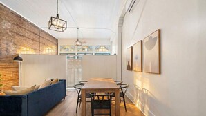 A dining area with a wooden table and chairs, a blue sofa, and a hanging light fixture.