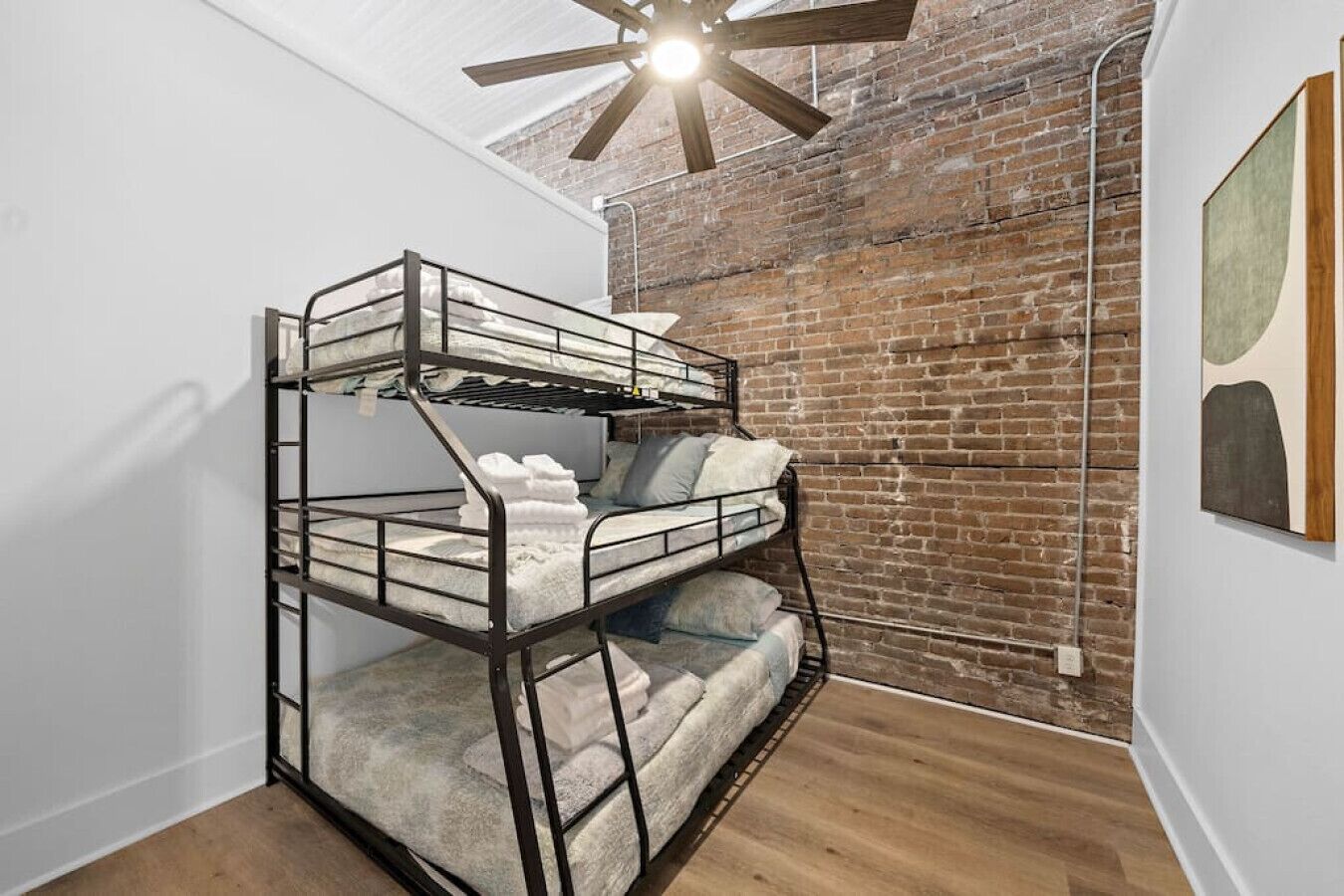 A bunk bed in a room with a brick wall and a wooden ceiling fan.