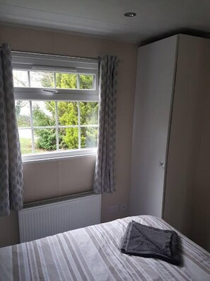 A bedroom with a bed, a radiator, a window with curtains, and a wardrobe. - Lovely 2-bed Chalet at Robinhood Retreat Free Park (Newark)