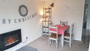 A cozy living room with a fireplace, a dining table with chairs, and a Christmas wreath on the wall. - Lovely 2-bed Chalet at Robinhood Retreat Free Park (Newark)