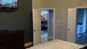 A bedroom with a bed, dresser, ceiling fan, and a TV mounted on the wall.