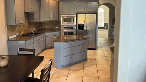 A modern kitchen with grey cabinets, a central island, a dining table, and a refrigerator.