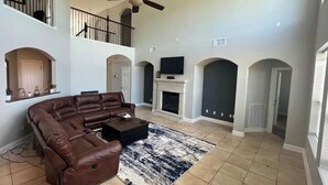 A spacious living room with a large sectional sofa, a fireplace, a ceiling fan, and a TV mounted above it.