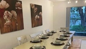 Ein Essbereich mit einem langen Tisch, gedeckten Plätzen für sechs Personen, weißen Stühlen und zwei Bildern an der Wand.