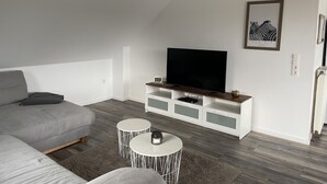 Una sala de estar moderna con un sofá gris, un televisor de pantalla plana sobre un mueble blanco, dos mesas redondas y un cuadro en la pared.