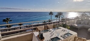 Ein Balkon mit Esstisch, der auf einen Strand und den Ozean blickt.