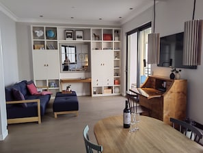 Ein modernes Wohnzimmer mit einer Couch, einem Hocker, einem Holzessttisch und einem großen Fenster.