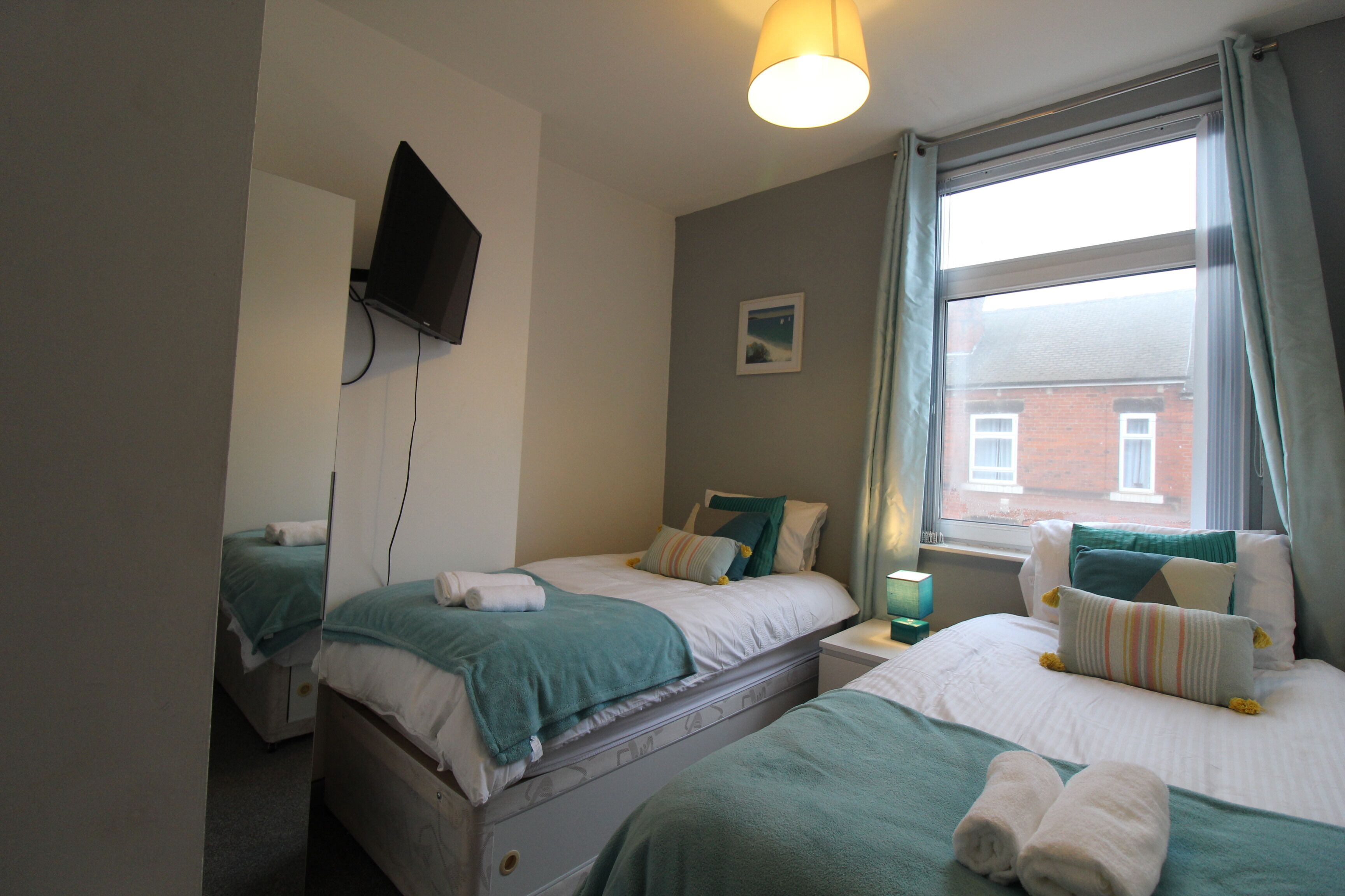 A hotel room with two beds, a television mounted on the wall, a window with curtains, and a small picture on the wall.