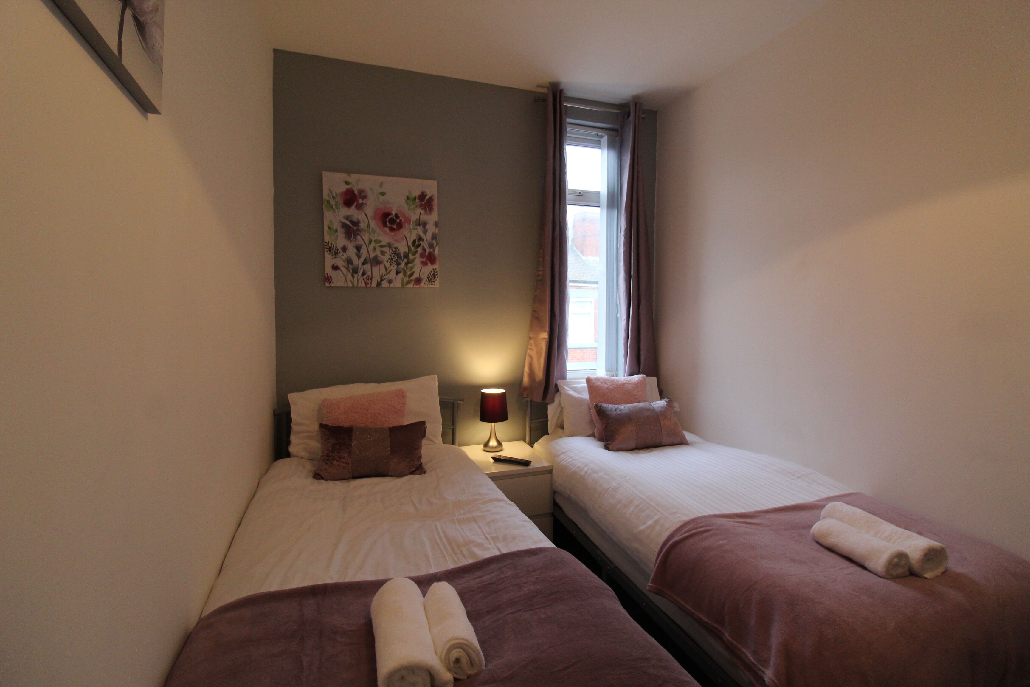 A hotel room with two beds, each with a brown blanket and rolled towels. There is a painting on the wall and a window with curtains.