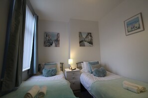 A hotel room with two beds, a nightstand with a lamp, and artwork on the walls. - Rockcliffe House (Rotherham)