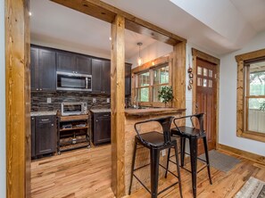 A kitchen with dark cabinets, a microwave, a toaster, and a wooden bar area with stools. - Biltmore Village · Fireplace · Treetop Porch (Asheville)