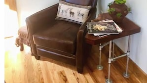 A corner room with a brown leather chair, a small table with a lamp, a framed mirror, and a wall art piece.