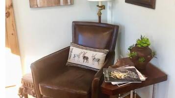 A corner room with a brown leather chair, a small table with a lamp, a framed mirror, and a wall art piece.