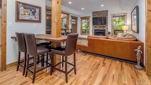 A dining area with a wooden table and chairs, a fireplace, and a sofa in a room with wooden flooring and a stone accent wall.