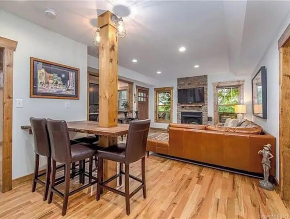 Un coin repas avec une table et des chaises en bois, une cheminée et un canapé, dans une pièce dotée d’un plancher en bois et d’un mur d’accent en pierre.