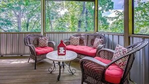 A covered outdoor seating area with wicker furniture and red cushions, a small round table, and a lantern.