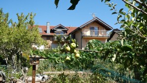Een woongebouw met balkon, omringd door weelderige begroeiing en fruitbomen.
