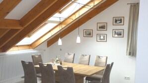 Een eetruimte met een houten tafel en zes stoelen, een dakraam en lijstwerken aan de muur.
