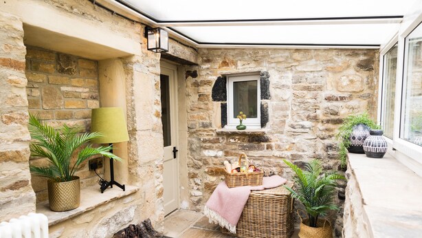 A stone-walled room with a window, a wicker basket, a potted plant, and a radiator.