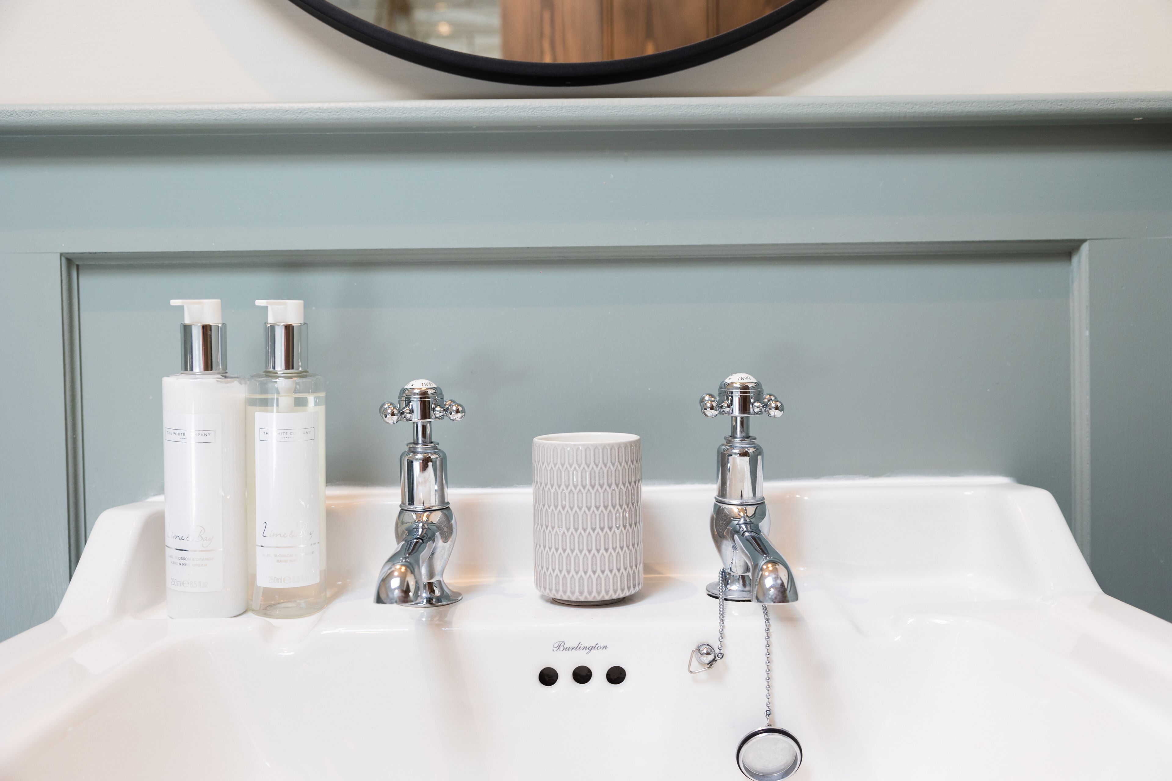 A bathroom sink with two bottles of liquid soap, a textured soap dish, and a ring-shaped soap dispenser.