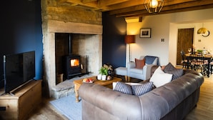 A cozy living room with a stone fireplace, a leather sofa, a flat-screen TV, and a dining area with a table and chairs.