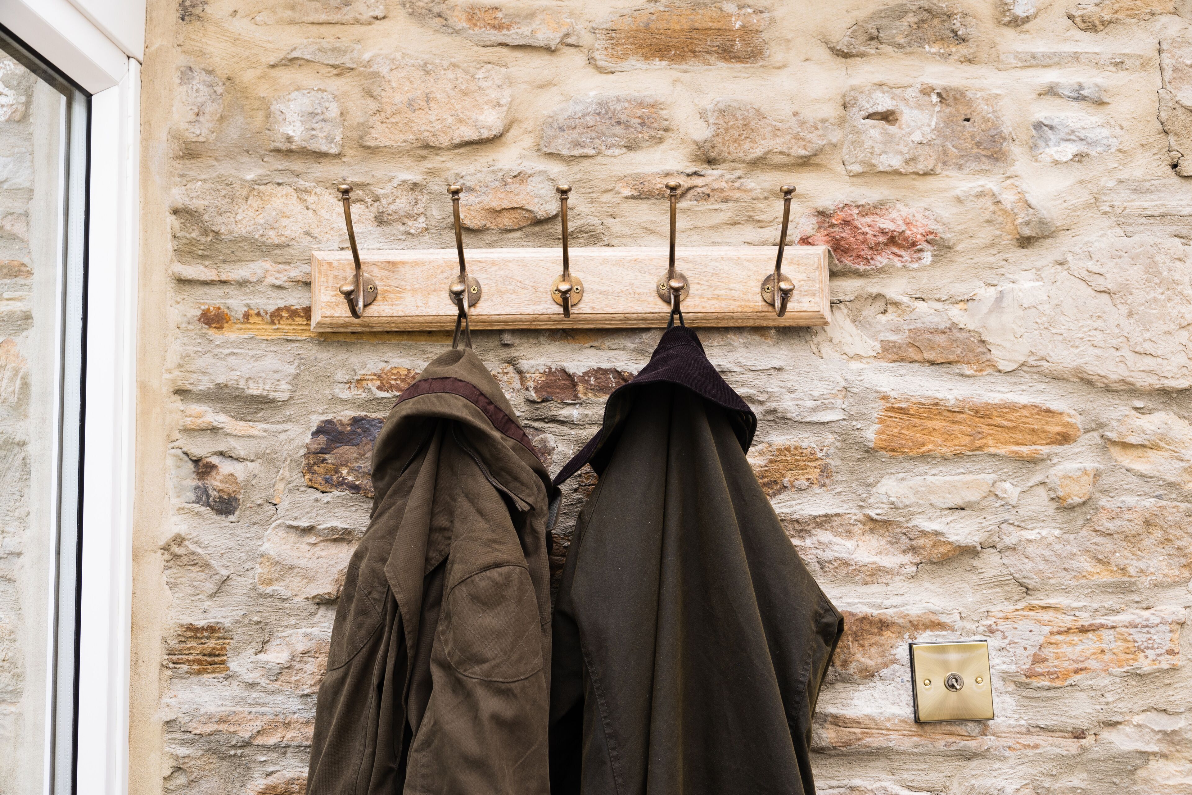 A stone wall with a coat rack holding two jackets.