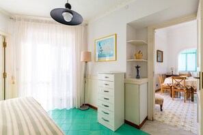 A bedroom with a bed, a desk, a lamp, and a dining area with chairs and a table.