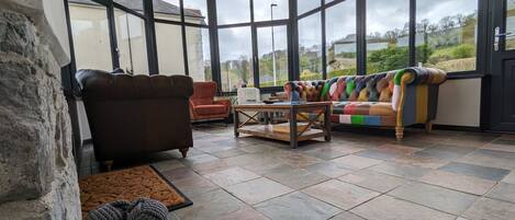 A corner room with large windows, a brown leather sofa, a colorful sofa, and a wooden coffee table.