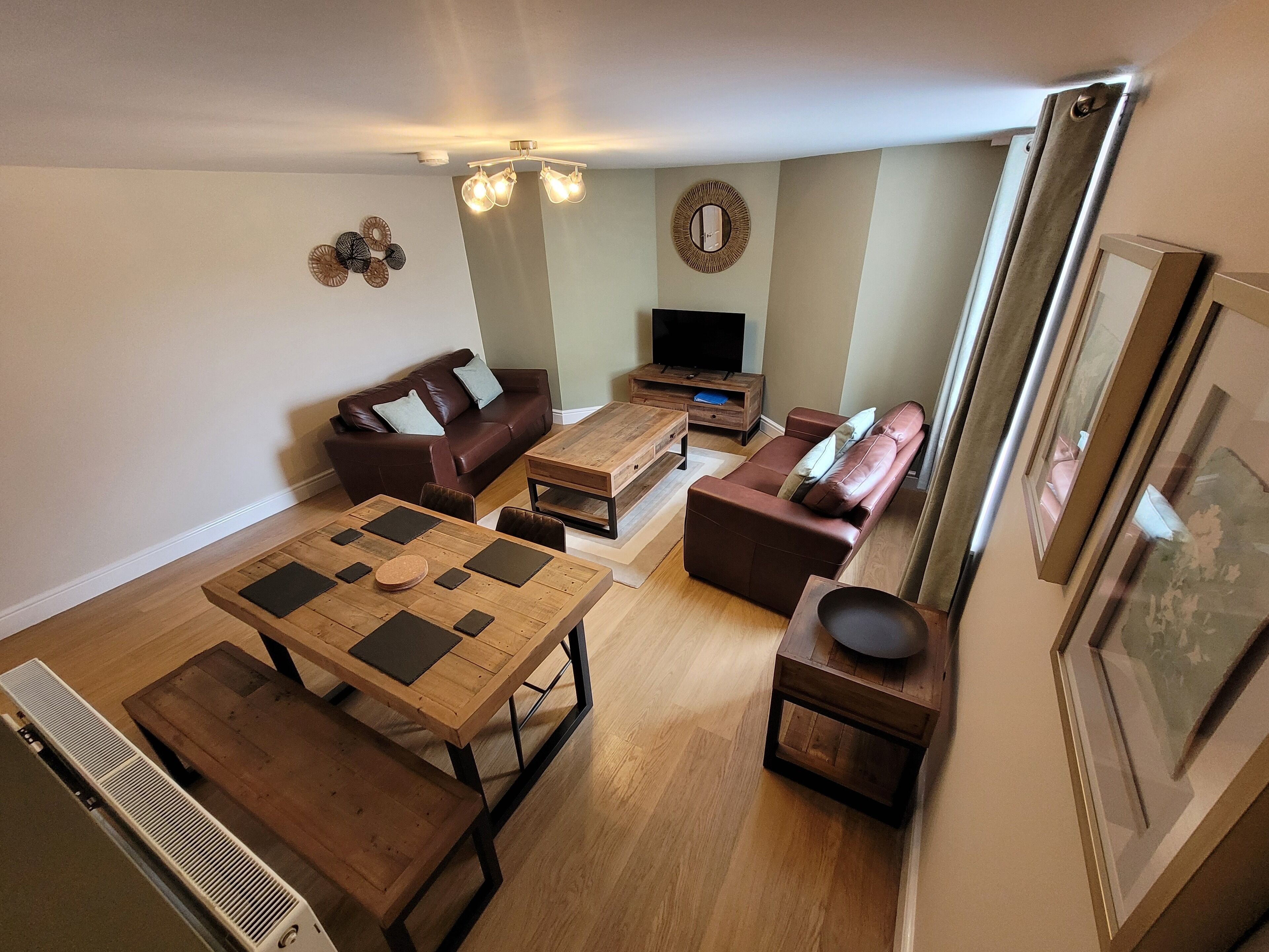 A living room with a wooden coffee table, two sofas, a TV stand, and a ceiling light fixture.
