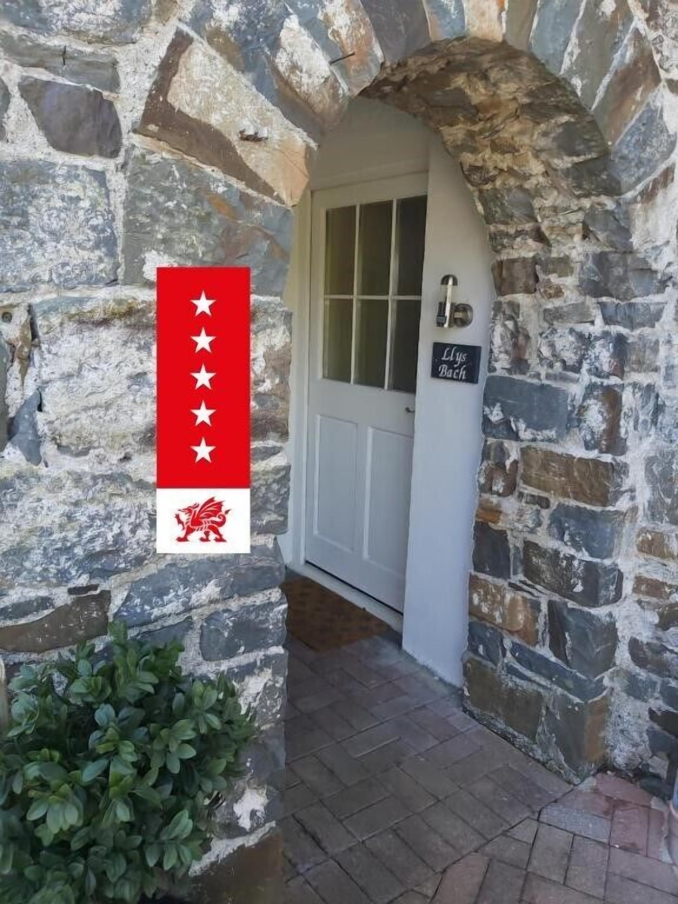 Ingresso di un edificio in pietra con una bandiera, una porta e un cartello che recita 'Lys Bach'.
