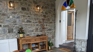 A cozy living room with a colorful sofa, a wooden coffee table, and a stone wall. - Llys Aeron Guest House (Aberaeron)