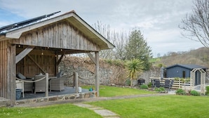 A rustic wooden building with a covered patio area, stone walls, and a fenced garden. - Llys Aeron Guest House (Aberaeron)