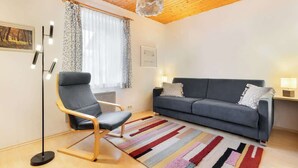 Un salon moderne avec un canapé gris, un fauteuil bleu, un tapis à rayures et un plafond en bois.