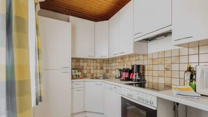 Une cuisine compacte avec des meubles blancs, un pare-feu en carrelage, une machine à café et un four à micro-ondes.