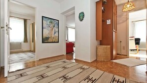 A spacious hallway with a patterned rug, a framed painting, and a coat rack.