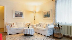 A living room with two white sofas, a round table, a floor lamp, and a radiator.