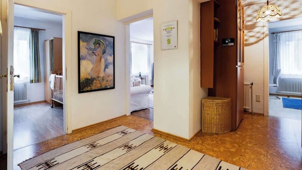 A hallway with a patterned rug, a framed painting, a certificate on the wall, and a wicker basket.