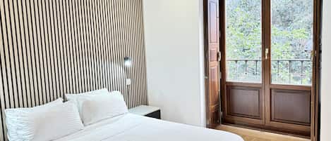 Un dormitorio con cama, cabecero de listones de madera, mesita de noche y ventana con vistas a zonas verdes.