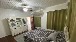 Ein Schlafzimmer mit Bett, Kleiderschrank, Deckenventilator und einem Fenster mit Vorhängen.