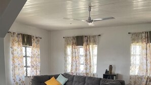 Ein geräumiges Wohnzimmer mit grauem Ecksofa, einem gemusterten Teppich und einem Deckenventilator.